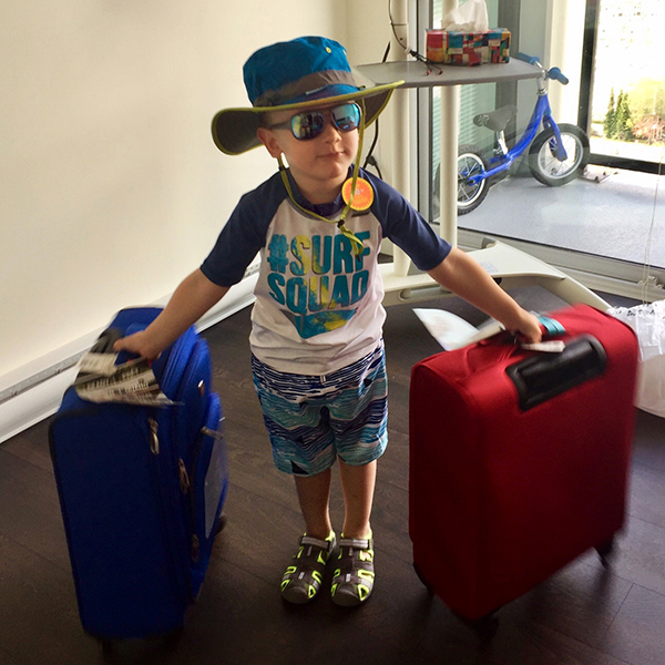 child in a travel hat and sunglasses with two suitcases ready to travel