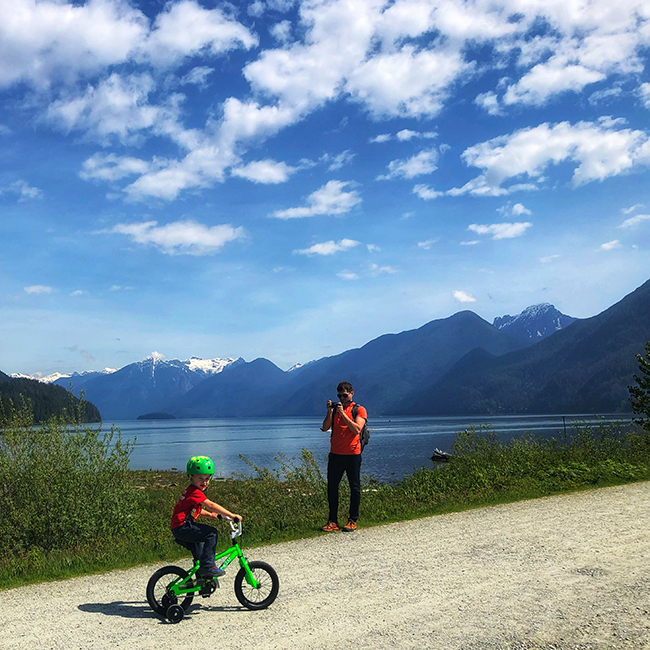 a father taking a photo of his son riding a bike at Rannie Road in Pitt Lake Ecological Reserve, near Pitt Meadows, BC