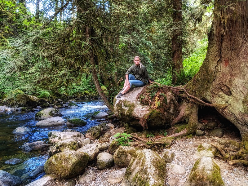 young woman sitting on a rock near a forest creek