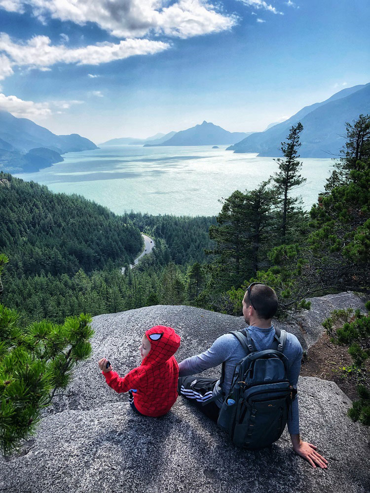 Father and child in Spider Man costume with the view of Howe Sound as seen from Jurassic Ridge hiking trail in Murrin Provincial Park BC Canada next to Squamish in the summer