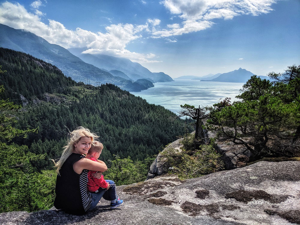 Mother smiling and hugging her child while they view Howe Sound from Jurassic Ridge hiking trail in Murrin Provincial Park near Squamish in BC Canada