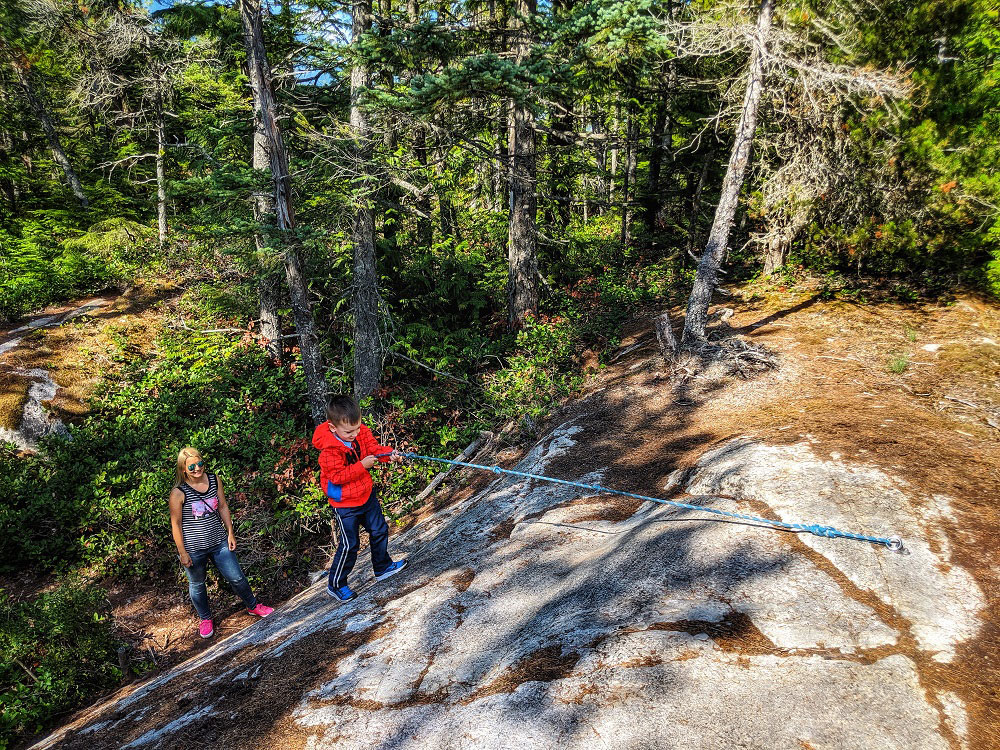 Mother and son using rope to hike up the Jurassic Ridge hiking trail in Murrin Provincial Park near Squamish in BC Canada