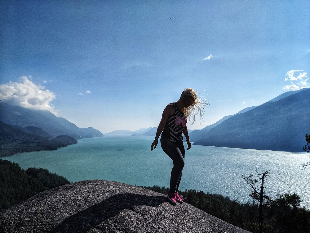 Blonde girl and the summer evening backdrop of Howe Sound as seen from Jurassic Ridge hiking trail in Murrin Provincial Park BC Canada next to Squamish