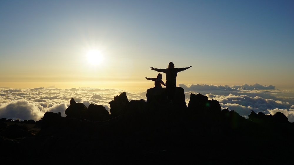 Mother and child "flying" above clouds watching sunset at Haleakala Volcano Summit in Maui Hawaii