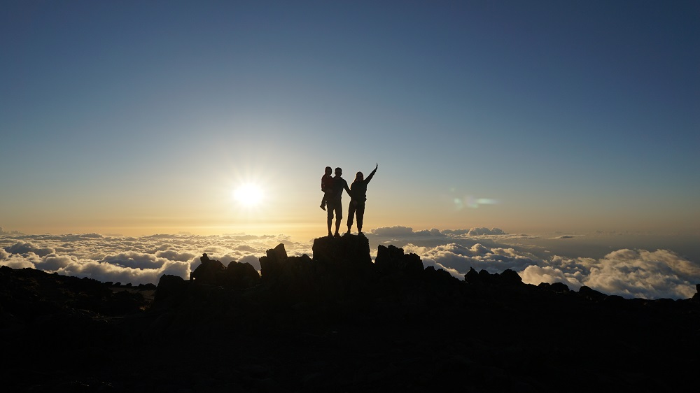 Stunning above-the-clouds sunset at Haleakala Summit in Maui Hawaii - family silhouette in front of a setting sun 