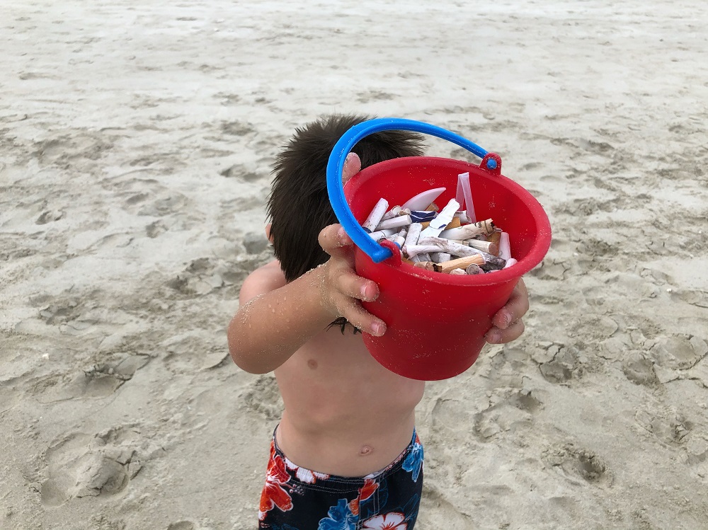 A Child with Red Sand-Bucket full of cigarette buds - beach pollution