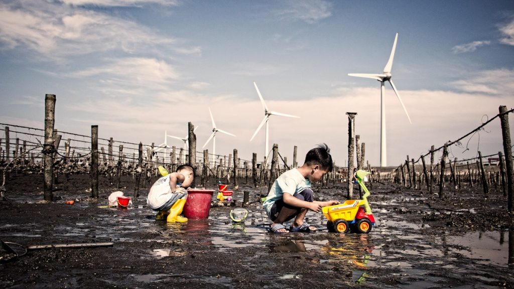 two children playing with toys in front of clean energy windmills. Teach kids sustainability practices early.
