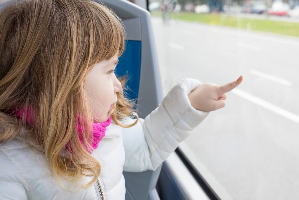 child on a bus pointing finger at a window - public transportation sustainability practice.