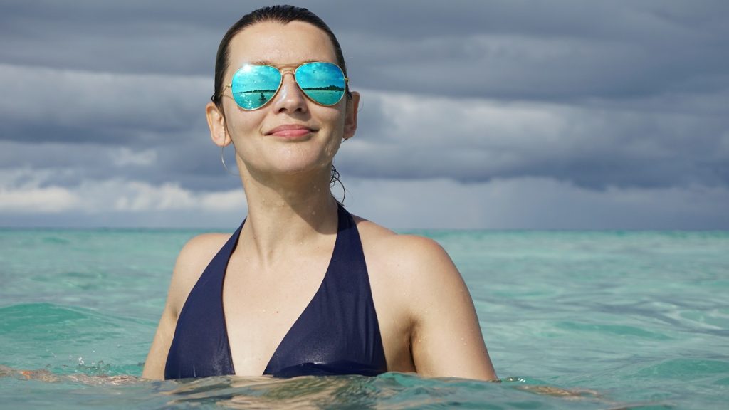 young woman in the water with sunglasses - what to bring to Cuba