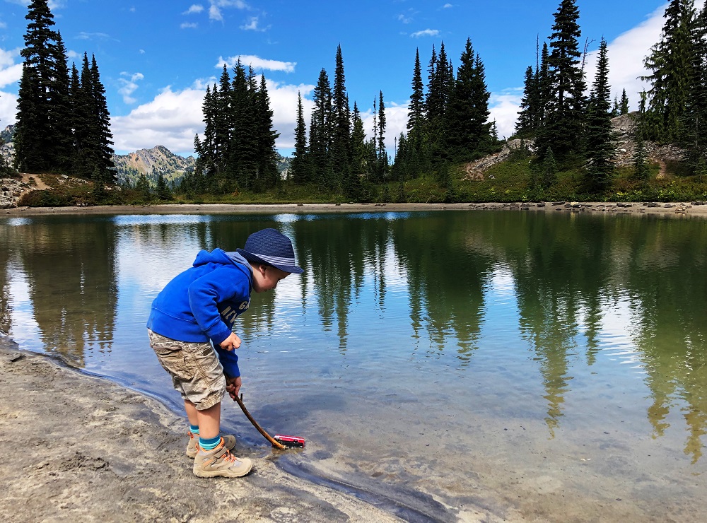 boy child in hiking shoes playing with water next to a mountain lake