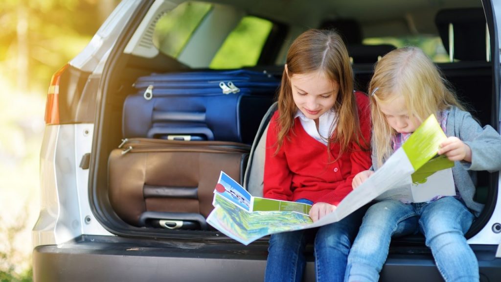 two girls looking at the travel map while sitting in a car trunk