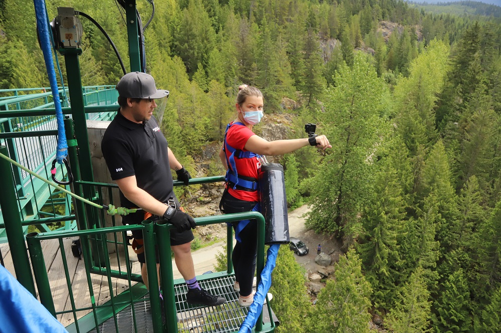 woman in a red tshirt wearing gopro on her hand standing at Whistler bungee bridge ready to jump