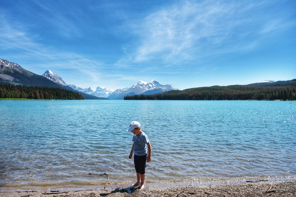child dipping feet in ice cold waters of Maligne Lake