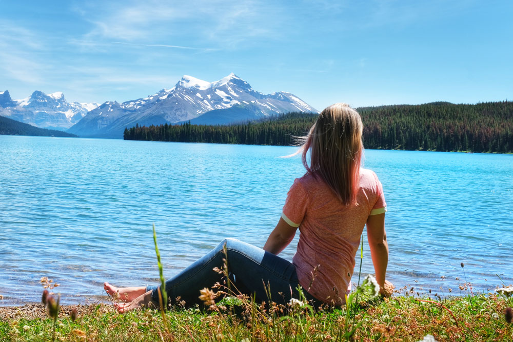 girl in pink shirt next to Maligne Lake in Jasper Alberta looking at the lake