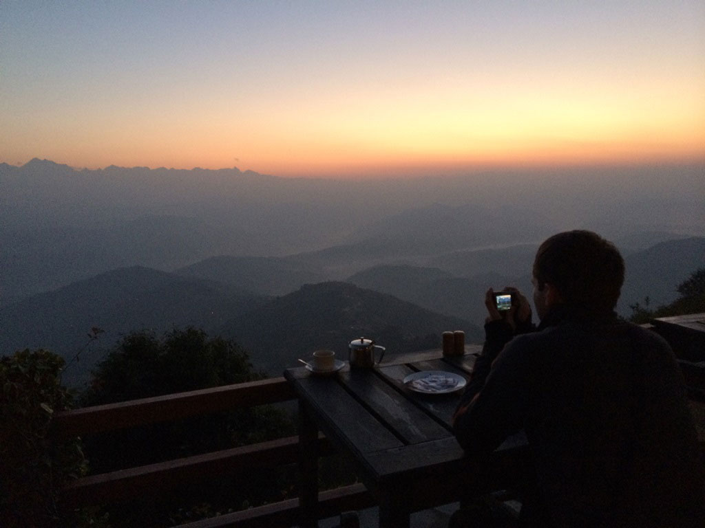 male tourist taking photos of sunrise at an outdoor patio in a hotel in Nepal