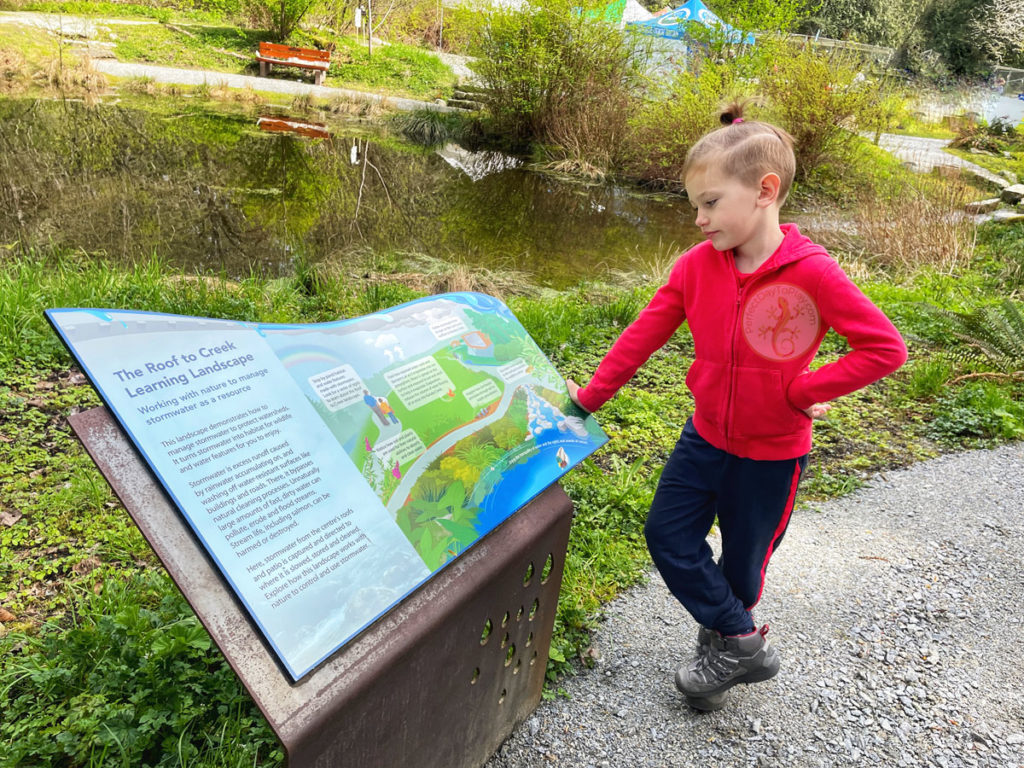 Child reading environmental signage near a pond
