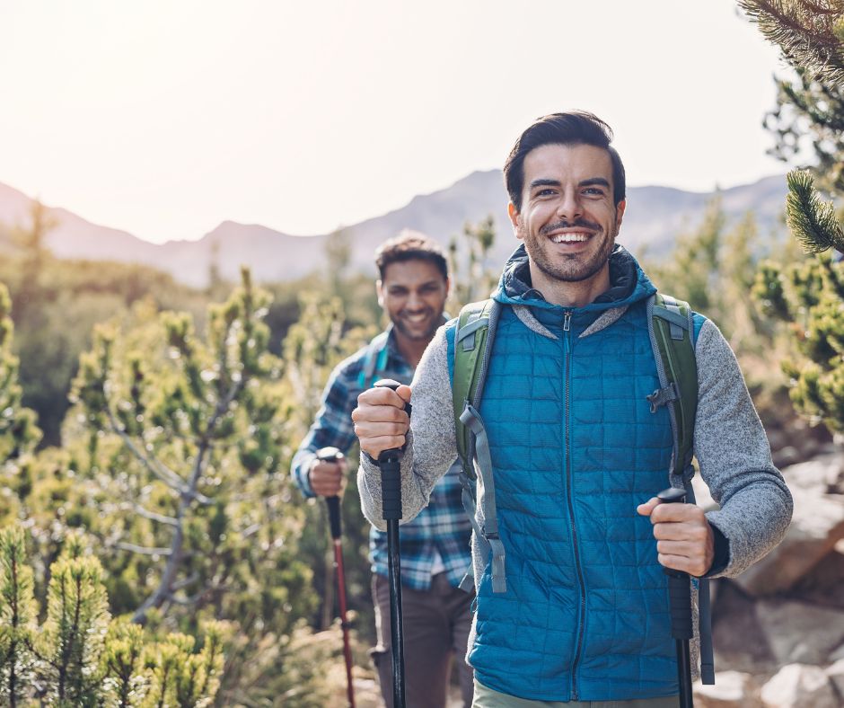 a pair of men smiling hiking on a trail