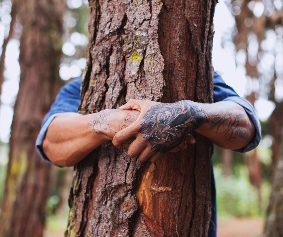man's tattooed hands hugging a tree